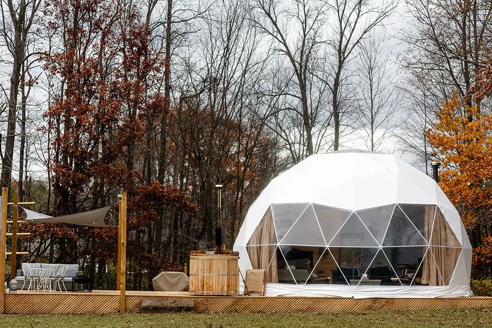 a geodesic dome used in glamping with an autumnal forest behind it.