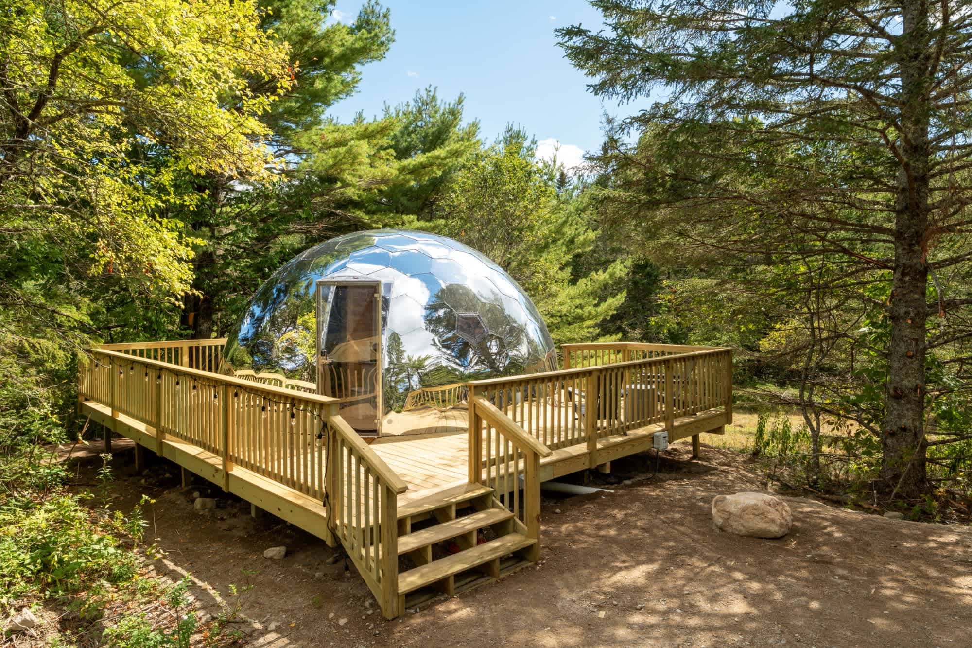A mirrored dome sits on a wooden deck in a woodsy area at Nature Nooks Acadia, where they had a glamping business build in 4 months.
