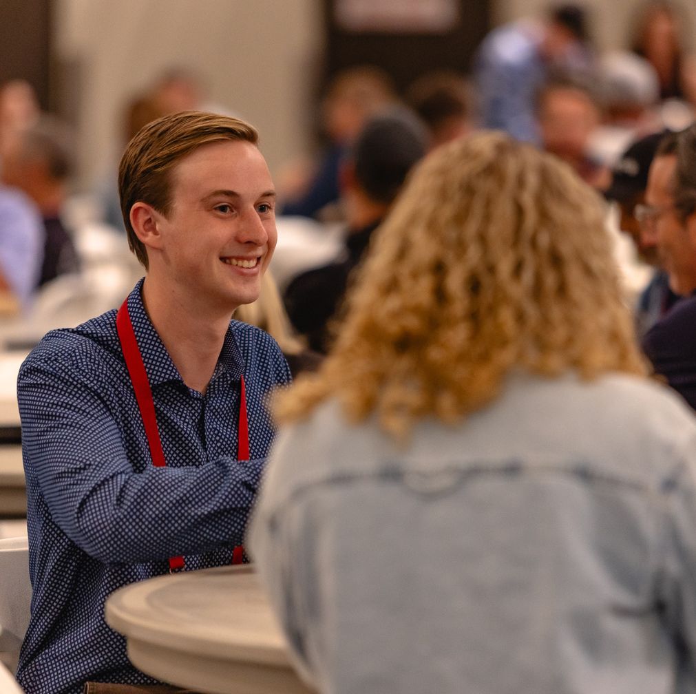 Glamping Show Americas networking at a conference table, with a smiling participant wearing a red lanyard engaged in conversation.