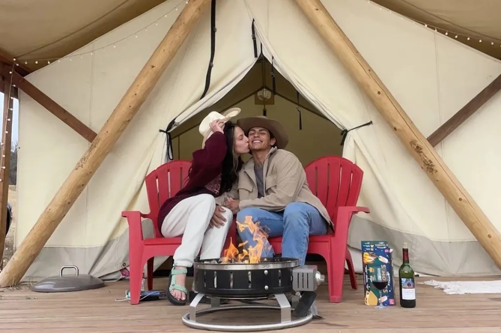 A couple snuggles by the campfire in front of a spacious glamping tent at Monument Glamping.